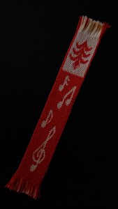 Woven bookmark in red and yellow, with musical notes, a treble clef and a pine tree