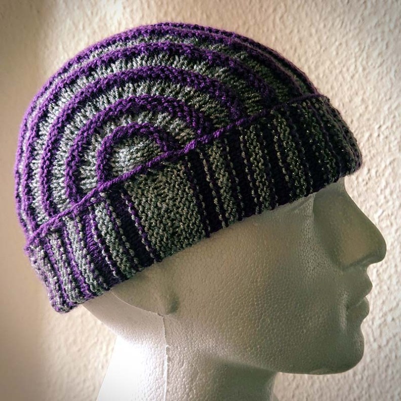 Striped cap knitted in dk  grey/black/cream/ color change yarn  and a contrasting purple yarn.
