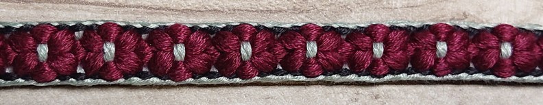 a braid with a black and blue border either side of  eight six-petaled flowers that have light blue centres. 