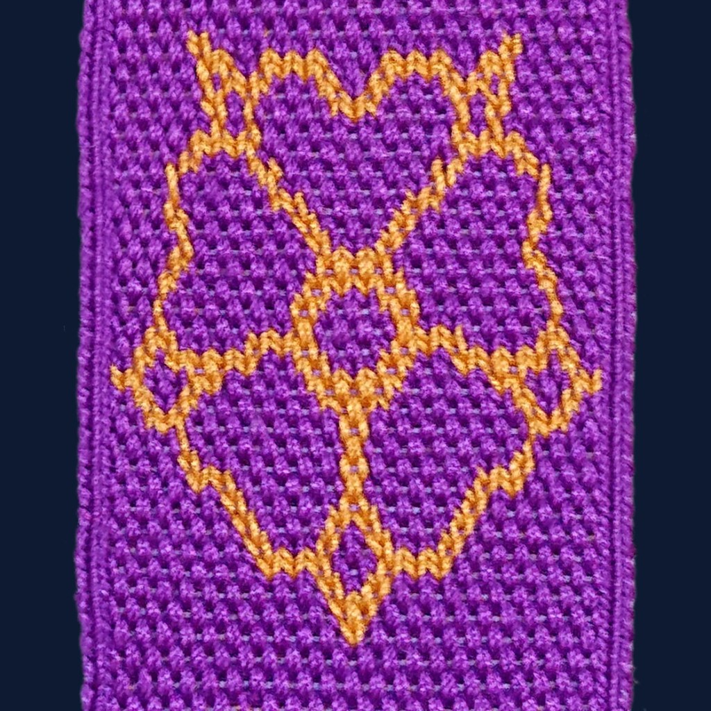 Close up of an outlined rose worked in double face tablet weaving.  The foreground is gold, and the background is purple. 